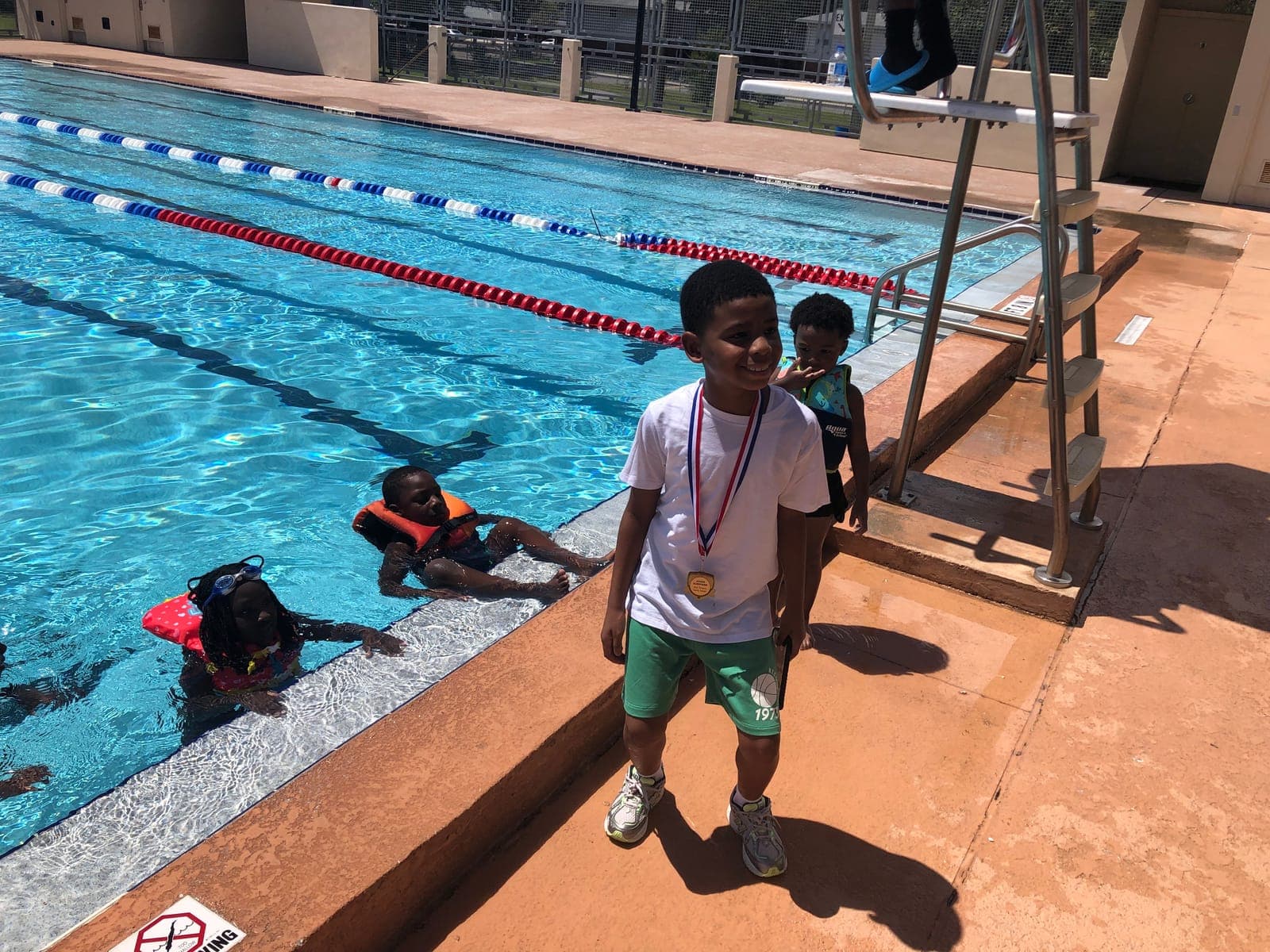 A young swimmer proudly wearing his medal at the pool deck